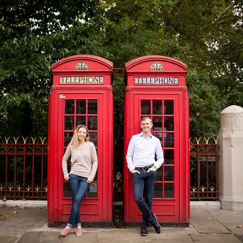 Two people in front of red telephone booths in London.