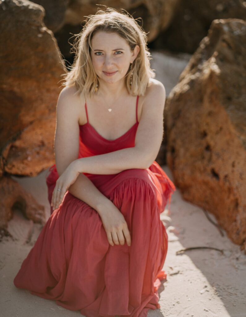 Jen smiling in red dress on a beach.